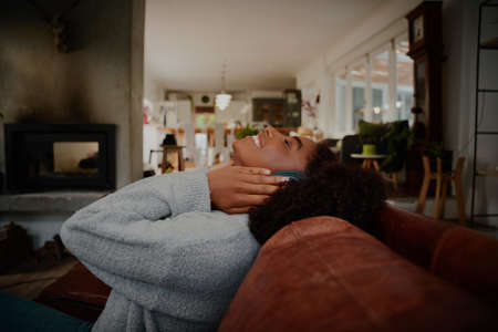 Happy african young woman sitting on sofa with headphones listening to music at home
