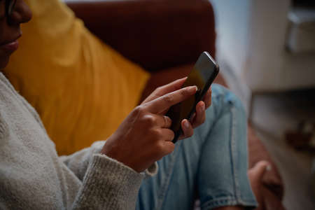 Closeup of young woman hand touching screen of mobile phone sitting on couch