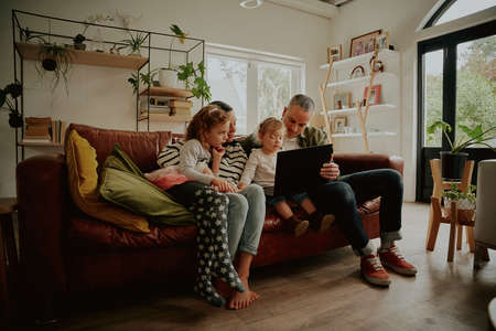 Young family with daughter watching video on laptop while relaxing at homeの写真素材