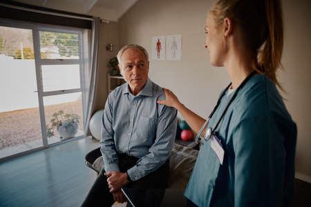 Young white female nurse consoling senior male patient in hospitalの写真素材