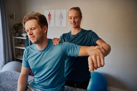 Young man suffering from hand injury doing stretching exercise with female physiotherapist
