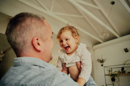 Portrait of little girl with wide open mouth enjoying on father lifting her in air while playing at homeの写真素材