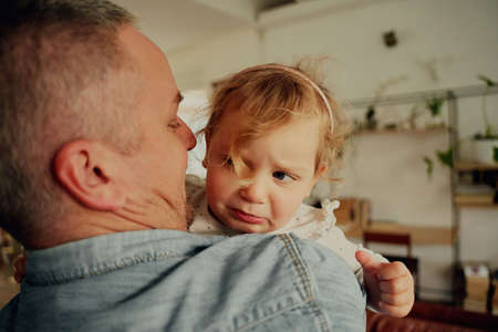 Portrait of upset little girl with hairband crying in fathers arms at homeの写真素材