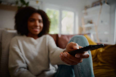 Closeup of woman hand holding remote control while sitting at home watching television aloneの写真素材