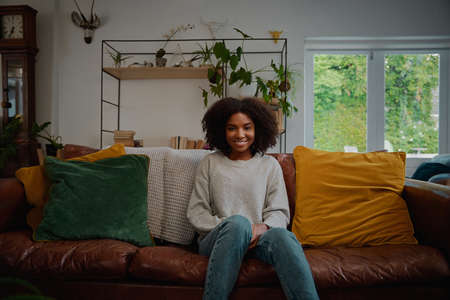 Portrait of beautiful woman with curly hair sitting on couch with cushionの写真素材