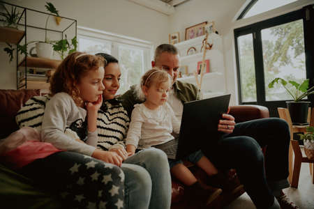 Young family children using laptop computer at home relaxing on couch