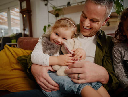 Happy father playing with daughter at home while sitting in couch at homeの写真素材