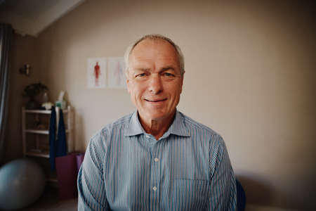 Portrait of smiling senior patient sitting in physiotherapy room looking at camera