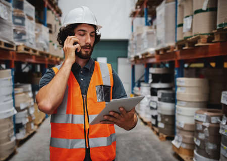 Warehouse manager tracking supply order details using digital tablet while in conversation over...