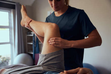 Closeup of young woman physiotherapist giving therapy treatment to patient on legの写真素材