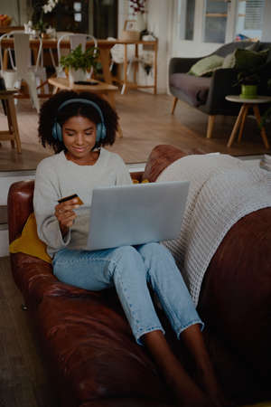 Young woman making an online payment with credit card relaxing at home on laptopの写真素材