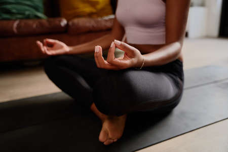 Closeup of hands of young woman sitting in lotus position meditating in the lotus pose at homeの写真素材