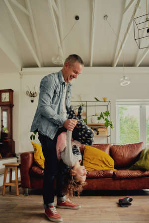 Father playing with daughter carrying her upside down at homeの写真素材