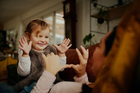 Playful child daughter having fun with mother lying on couch at homeの写真素材