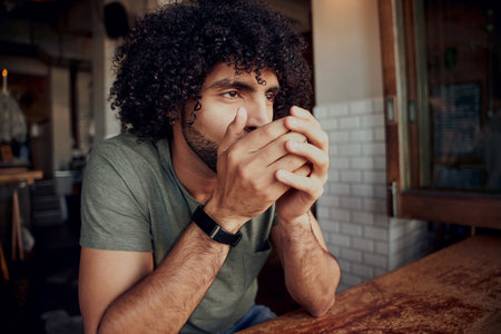 Handsome African American man with an afro drinking a coffee in a cosy coffee shopの写真素材