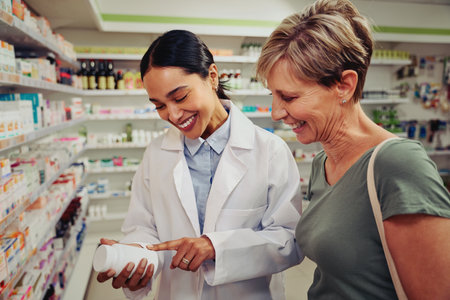 Smiling senior customer with pharmacist looking for medicinal details on bottle standing near shelvesの写真素材