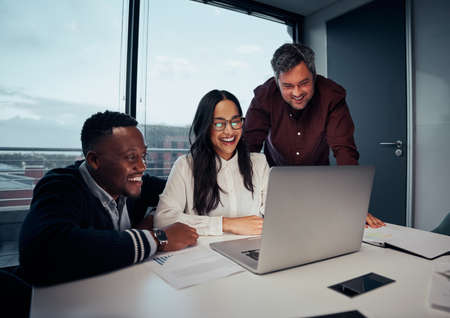 Happy multiethnic group of business people looking at laptop discussing new project in office