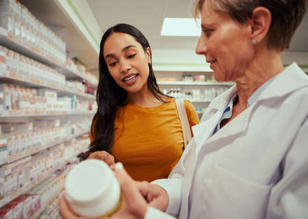 Young woman buying medicines in pharmacy with help of senior pharmacist standing near shelvesの写真素材