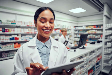 Happy woman working in medical store wearing labcoat using digital tabletの写真素材