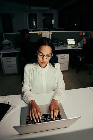 Portrait of a young female executive wearing eyeglasses typing on portable laptop at workplaceの写真素材