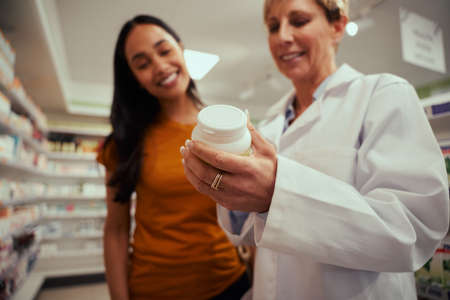 Closeup of hands of senior pharmacy woman helping female customer find bottle of medicine from shelvesの写真素材