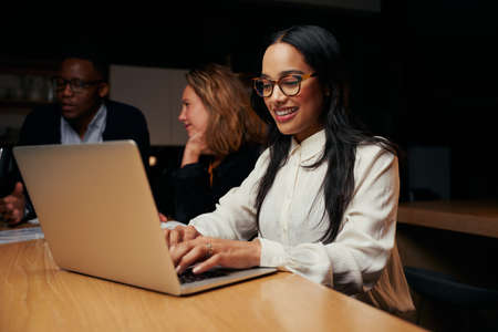 Smiling young businesswoman working on laptop in officeの写真素材