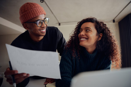 Close up of young mixed race couple using laptop for online banking. Happy African American couple smiling and looking at each other while working together at home. High quality photoの写真素材