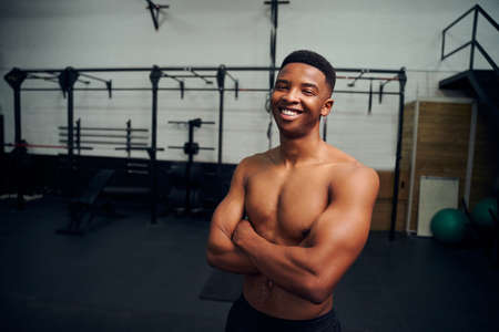 African American male standing with crossed arms and smiling to the camera. Male personal trainer...