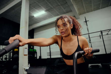 African American female using an elliptical trainer during cross fit training. Woman athlete working out in the gym. High quality photoの写真素材