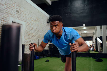 African American man working out intensely during cross fit training. Male athlete pushing the sled in the gym. High quality photoの写真素材