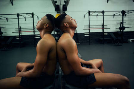 African American male athlete resting in the gym after a hard cross training. Shirtless mixed race male sitting down after exercising. High quality photoの写真素材