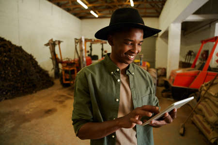 Mixed race male farmer typing on digital tablet standing in shed smiling. High quality photoの写真素材