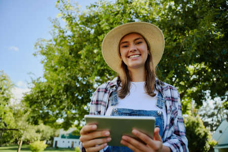 Caucasian female farmer standing outdoors typing on digital tablet researching for assignment . High quality photoの写真素材