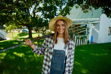 Caucasian female farmer standing in front of farm house ready to work holding pitchfork. High quality photoの写真素材