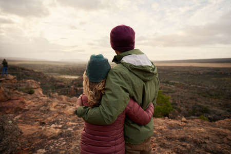 Rear view of young couple in love embracing while looking at beautiful landscape nature standing at...