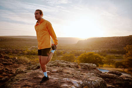 Young man athlete doing running warm-up before running in nature