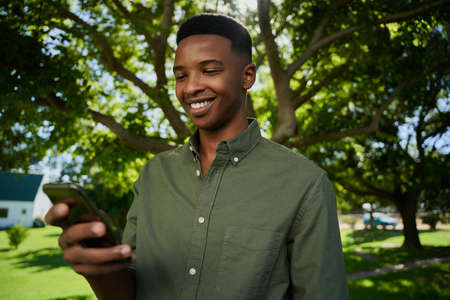 Mixed race male farmer standing outdoors smiling at cellular device texting friends. High quality...