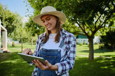 Caucasian female farmer standing outdoors typing on digital tablet completing assignment . High quality photoの写真素材