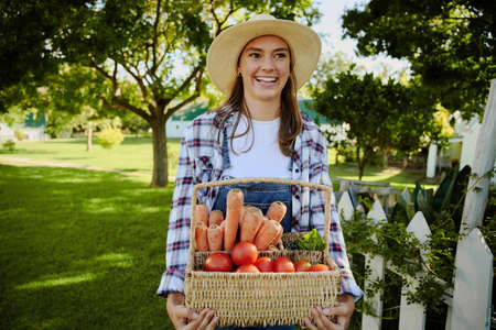 Caucasian female farmer walking outdoors with basket fo fresh vegetables . High quality photoの写真素材