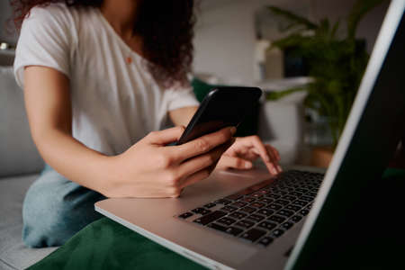 Close up of hands of a mixed race female typing on laptop and looking at phoneの写真素材
