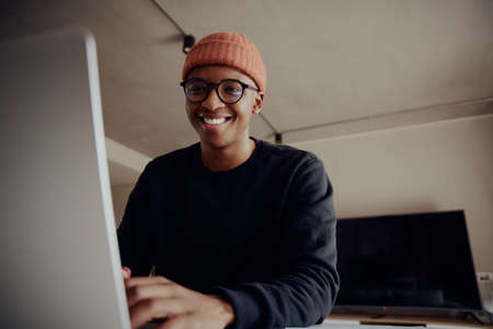 Black male smiling at camera while on laptop sitting at kitchen counter. Adult work from home.の写真素材