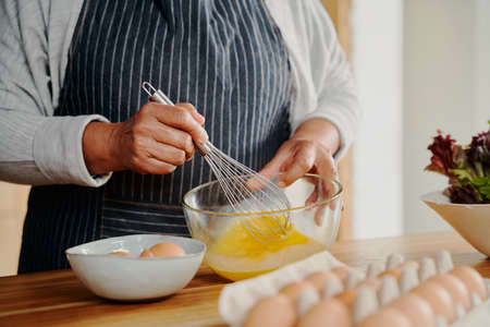 Close up of hands, elderly multi-cultural female whisking eggs for breakfast. Retired at home.