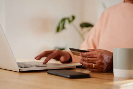 Hands of elderly multi-ethnic female making online payment on laptop, sitting at counter.