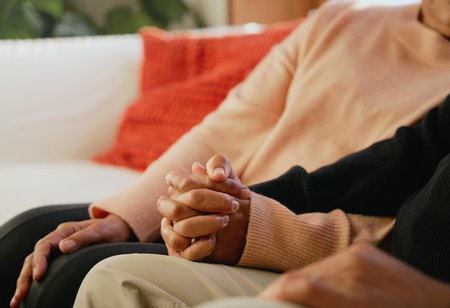 Close up of multi-cultural elderly couple holding hands on living room sofa. High quality photo