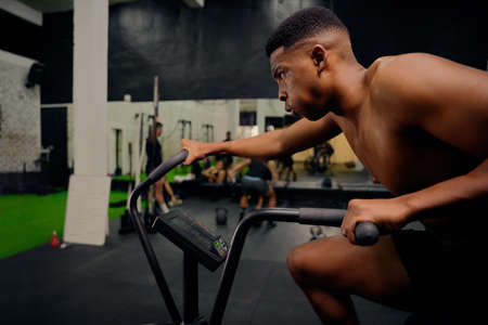 African American male using an elliptical trainer during cross training. Male personal trainer...
