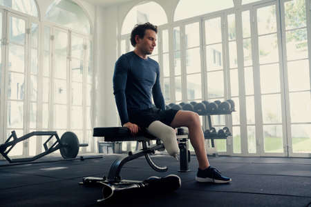 Man with prosthetic leg sitting on a gym bench . He is mentally preparing for his training session