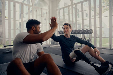 Two friends training in the gym - one with a prosthetic leg . Two men high fiving in the gym after a...