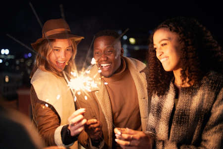 Group of Multi-cultural young adults lighting sparklers. Friends at a party on a rooftop in the city. High quality photoの写真素材