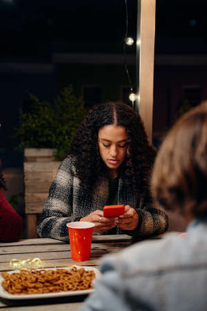 Biracial young adult female sitting at party, texting on her phone. Anti-social, using technology at...