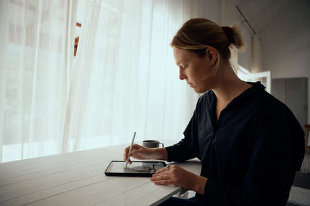 Caucasian female fashion designer creating art from home on digital tablet working from home. High...